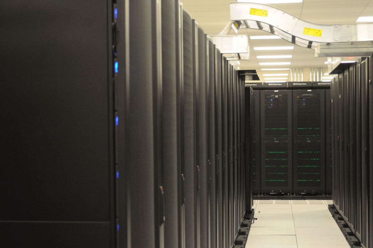 Rows of black server racks in a data centre aisle with green status lights