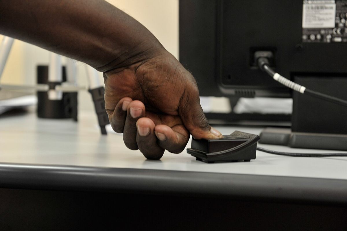 A hand pressing a fingerprint scanner next to a computer monitor.