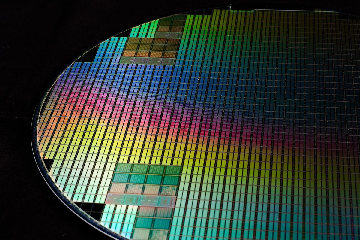 Silicon wafer with rows of chips reflecting a rainbow of colours against a black background