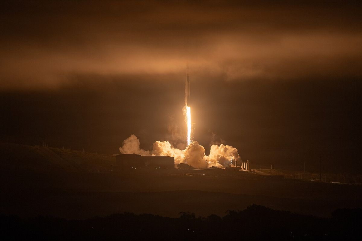 A SpaceX Falcon 9 rocket lifting off at night from Vandenberg Space Force Base, lighting the clouds orange